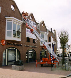 Materiaal wordt met een ladderlift naar het dak van een winkelpand gebracht